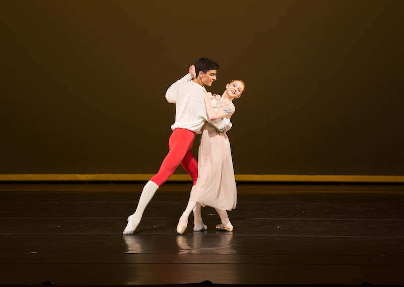 Two Dancers hold one another as if they are going to engage in a waltz. His foot points behind him while her foot points to the front. 
